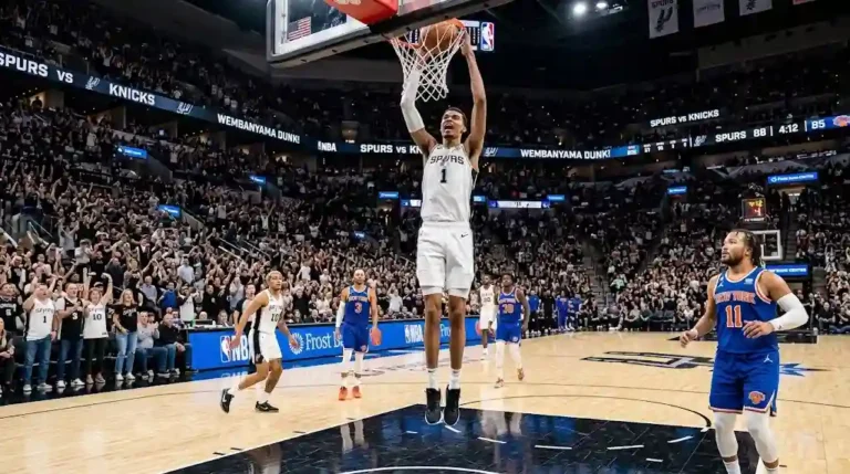 Victor Wembanyama in a white San Antonio Spurs jersey soaring high to dunk a basketball into the net, while Jalen Brunson and other players watch on the hardwood court during an NBA game against the New York Knicks.