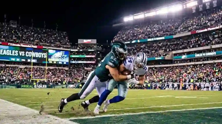 A Philadelphia Eagles player tackling a Dallas Cowboys ball carrier on the field in a packed NFL stadium at night under bright stadium lights.