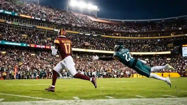 Washington Commanders player in a burgundy jersey mid-sprint while a Philadelphia Eagles defender in midnight green lunges toward him during an NFL night game